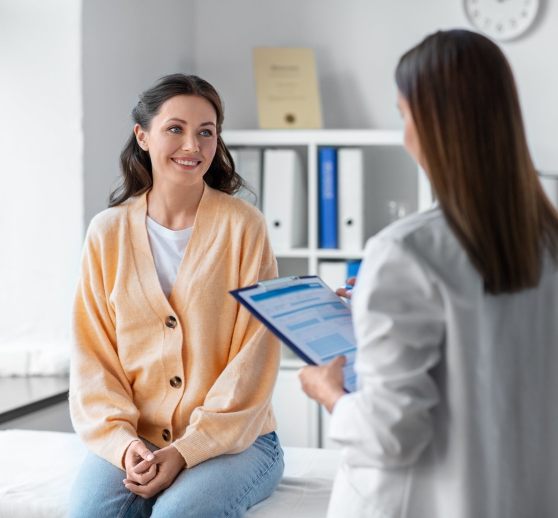 Female doctor with clipboard talking to smiling woman patient at hospital