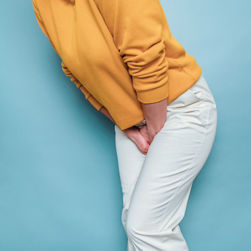 A woman hunched over with her hands between her legs pressing on her bladder in pain