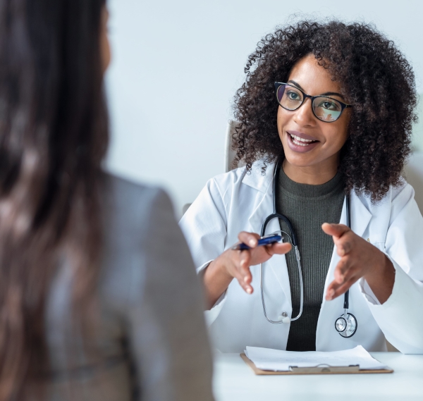 Beautiful cheerful female doctor talking while explaining medical treatment to patient in the consultation.