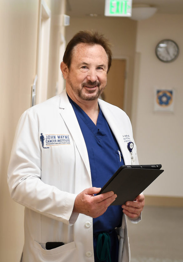 Dr Steven Vasilev MD standing in hallway holding medical tablet, looking at camera and smiling
