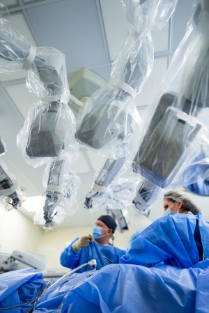 A male and female physician in scrubs performing surgery in the OR with 3 robotic arms from the da Vinci robotic surgery machine in the foreground