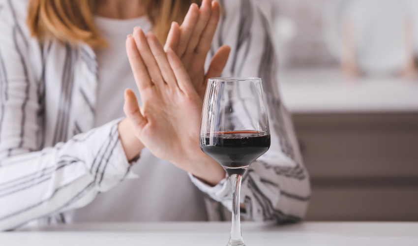 White woman with hands crossed saying no to glass of wine