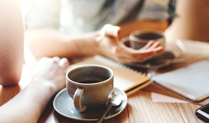 Close up of two womens hands next to their cups of coffee while having a discussion