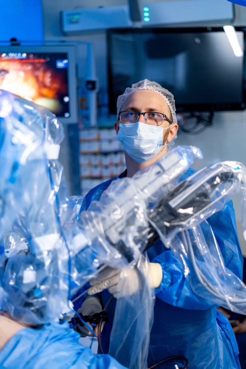 Surgeon using robot in hospital. A surgeon in blue scrubs performs robotic surgery in a modern operating room, concentrating on the equipment.
