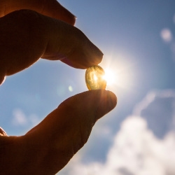 A hand holding up a vitamin D supplement pill obscuring the sun.
