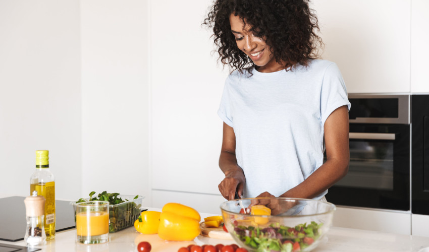 Young black woman smiling while preparing healthy meal of fruits and vegetables