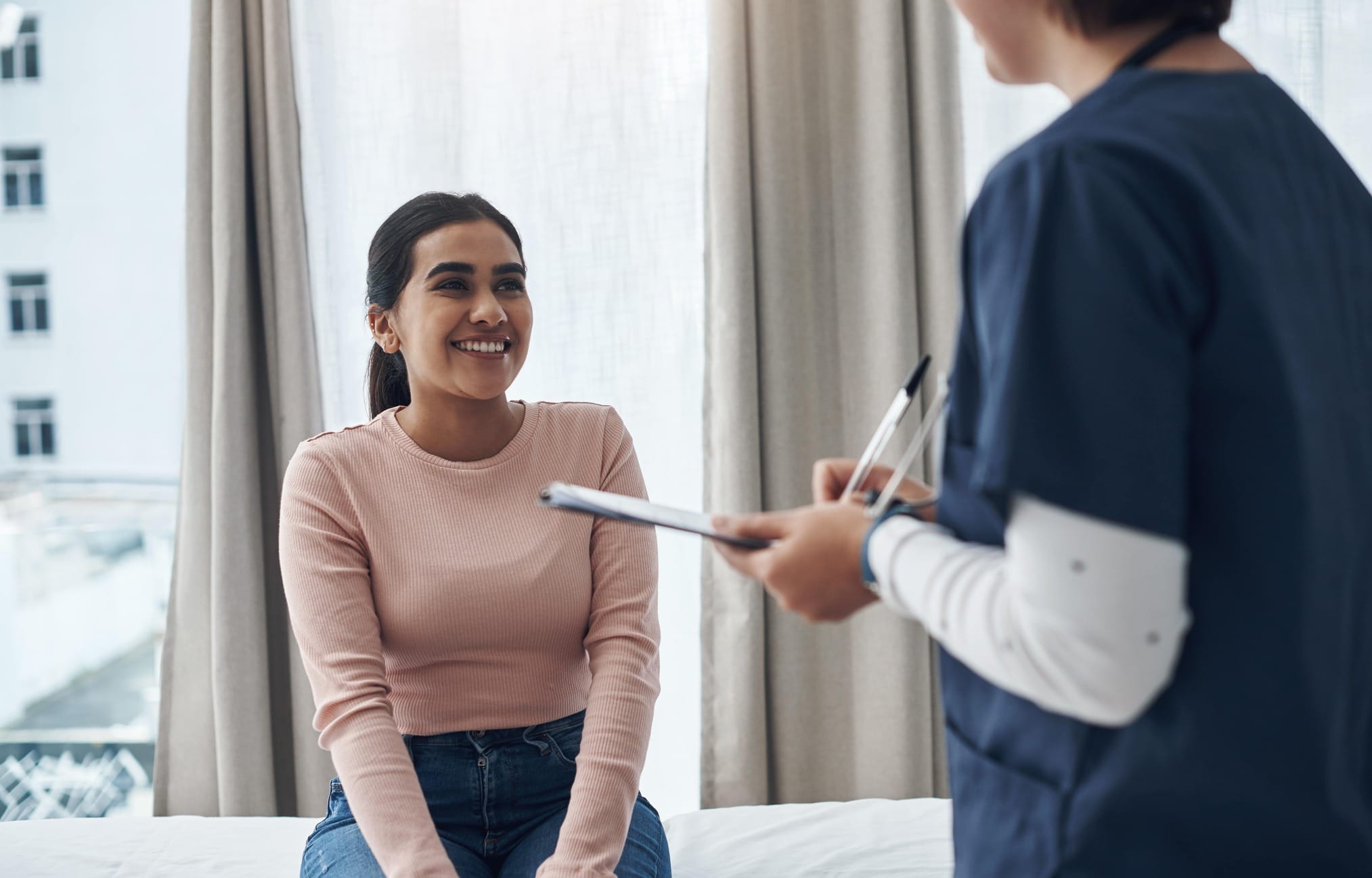 Female nurse writing down female patient's information on clipboard while patient smiles.