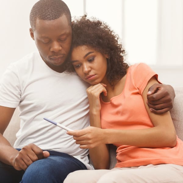 Couple embracing and appear somber while looking at pregnancy test