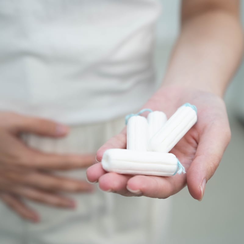 A woman holding her lower abdomen with one hand with the other held out with 4 tampons in her palm