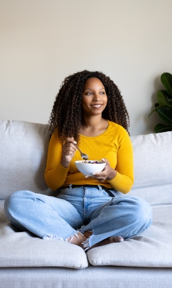 A black woman happily sitting on a couch enjoying a meal without pain