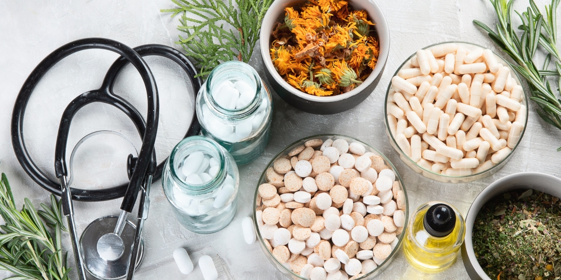 Top down view of various vitamins, herbs, and supplements, a stethoscope lay beside them