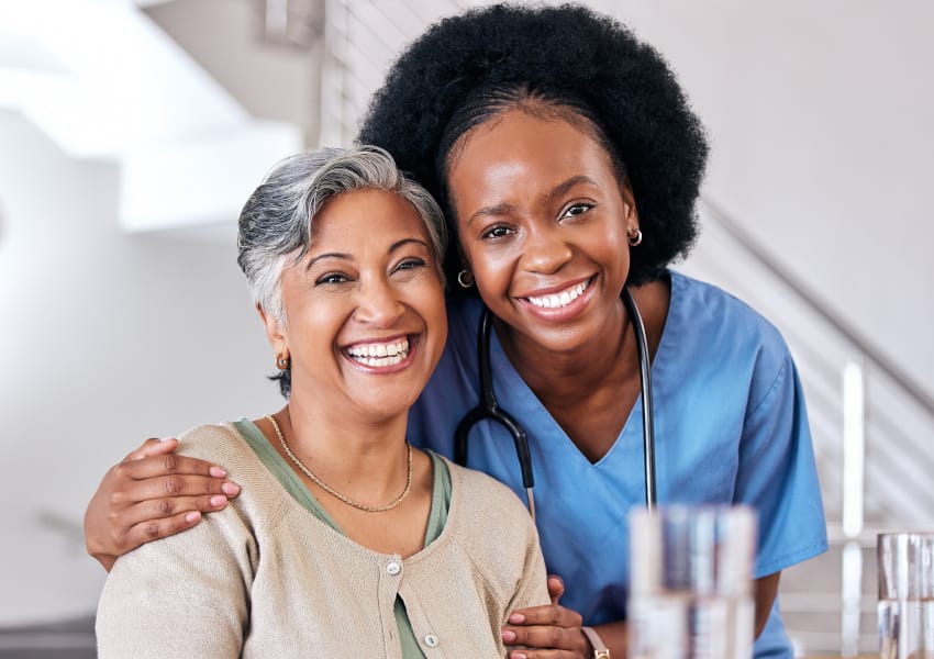 A female nurse leaning into next to a female patient, smiling at the camera